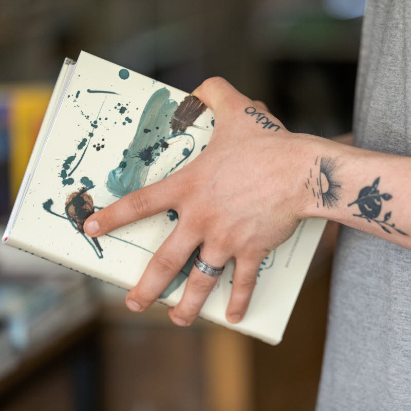 Tatuerade armar som håller i en bok.