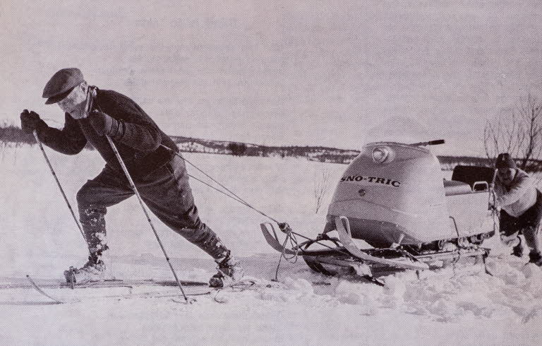 Man på arkivfoto på skidor som drar en skoter. 