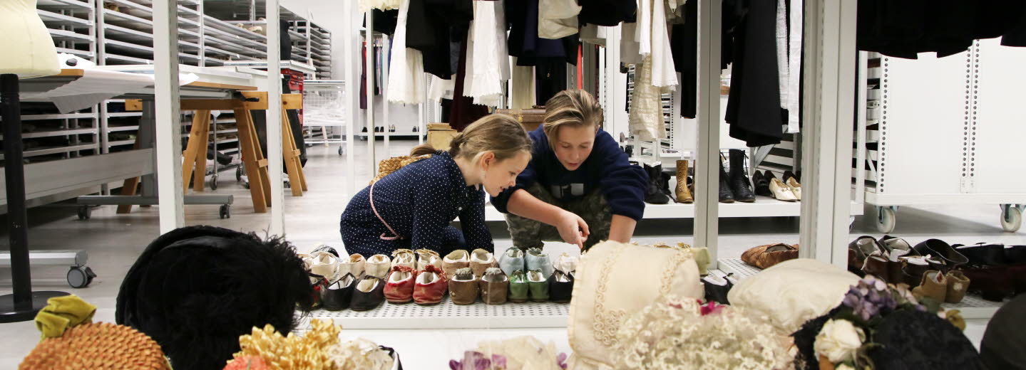 Två barn, pojke och flicka, i museums magasin pekar på samling skor.