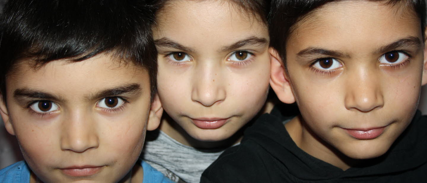 Foto på tre barn, de tittar in i kameran med skarp och nyfiken blick.