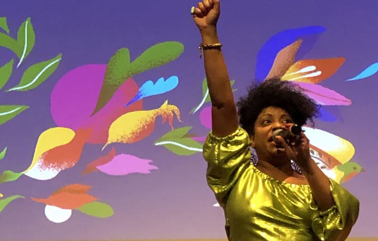 Kvinna som håller en mikrofon i handen och ströcker upp ena handen i luften.