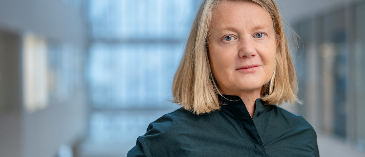 Medelålderskvinna i halvfigur. Blond page och mörkblå blus. 