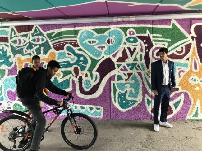 Ungdomar med cykel framför graffitti-målad tunnelvägg.