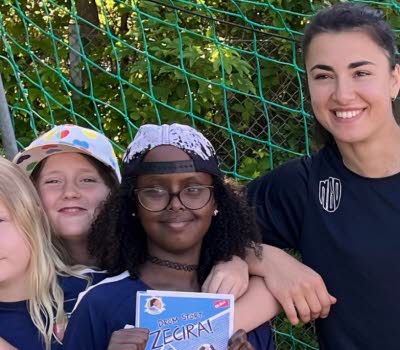 Barn i fotbollskläder som poserar tillsammans med en kvinna i ett fotbollsmål.