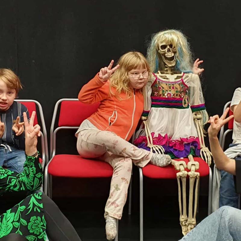 Två pedagoger och tre barn poserar med ett pyntat skelett.