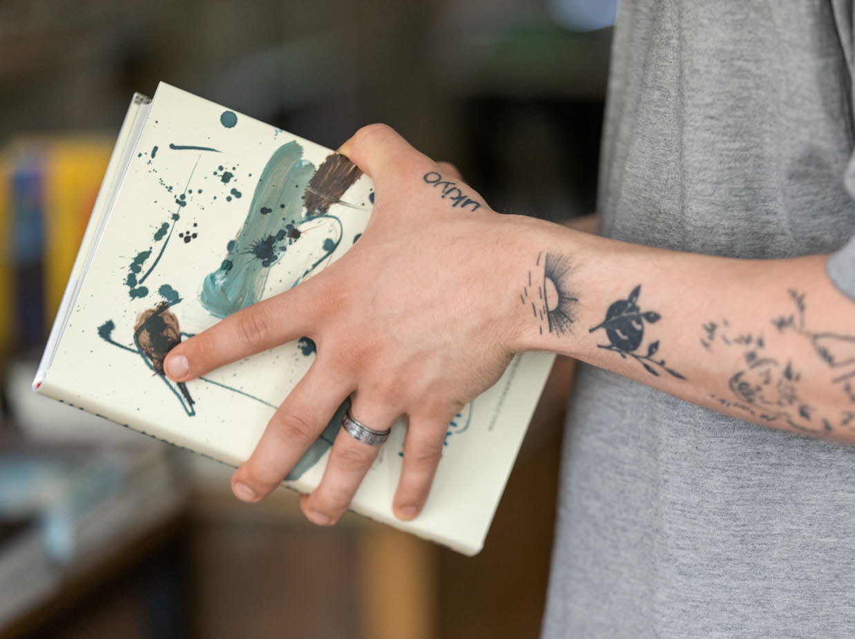 Tatuerade armar som håller i en bok.