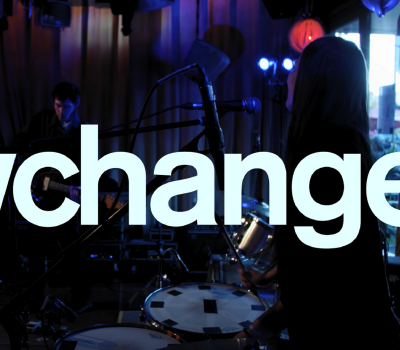 Vit text med Keychange, i bakgrunden ett band som spelar.