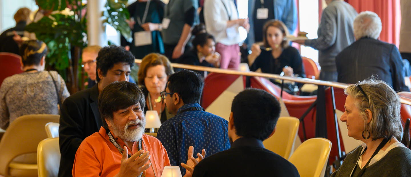 Fullsatt rum med människor som pratar i sittgrupper runt olika bort.