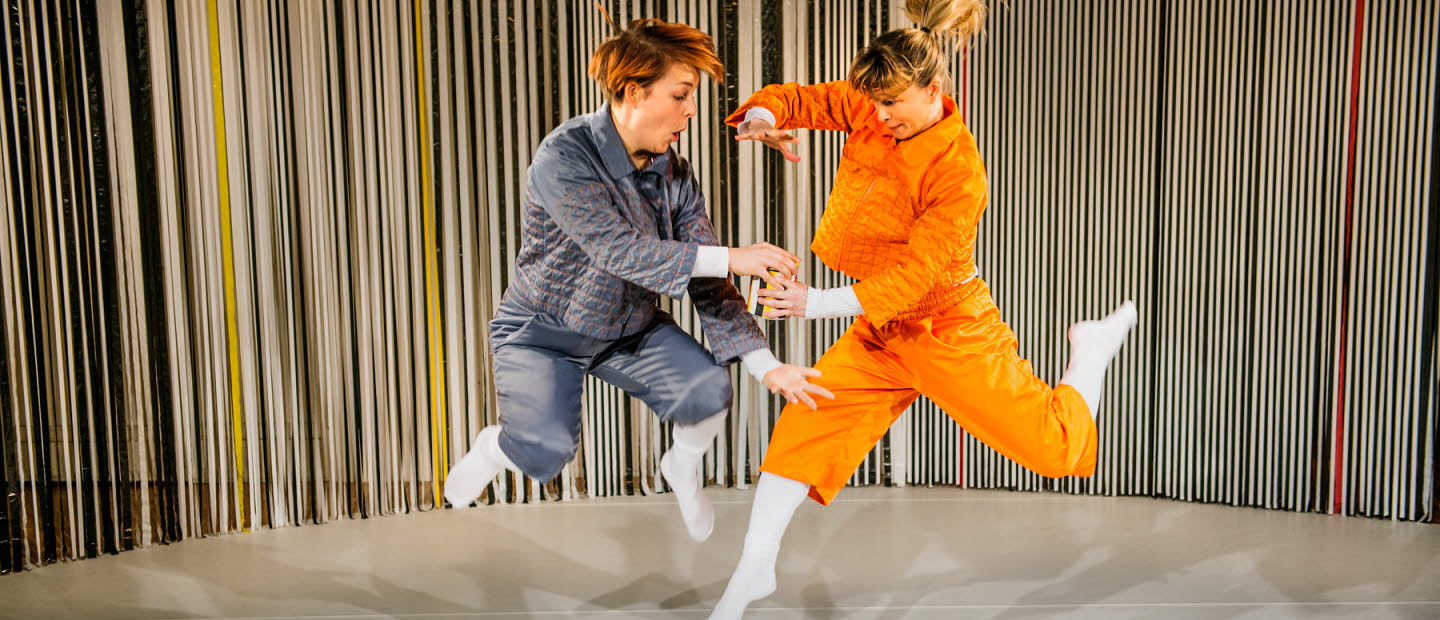 Två dansare som hoppar och samtidigt håller om en burk. 