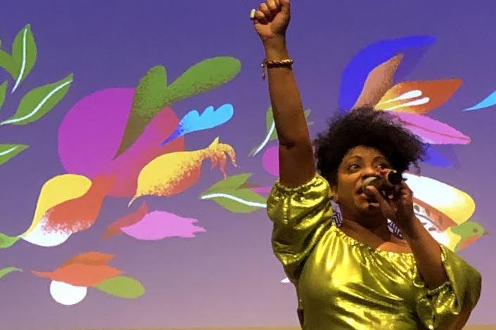 Kvinna som håller en mikrofon i handen och ströcker upp ena handen i luften.