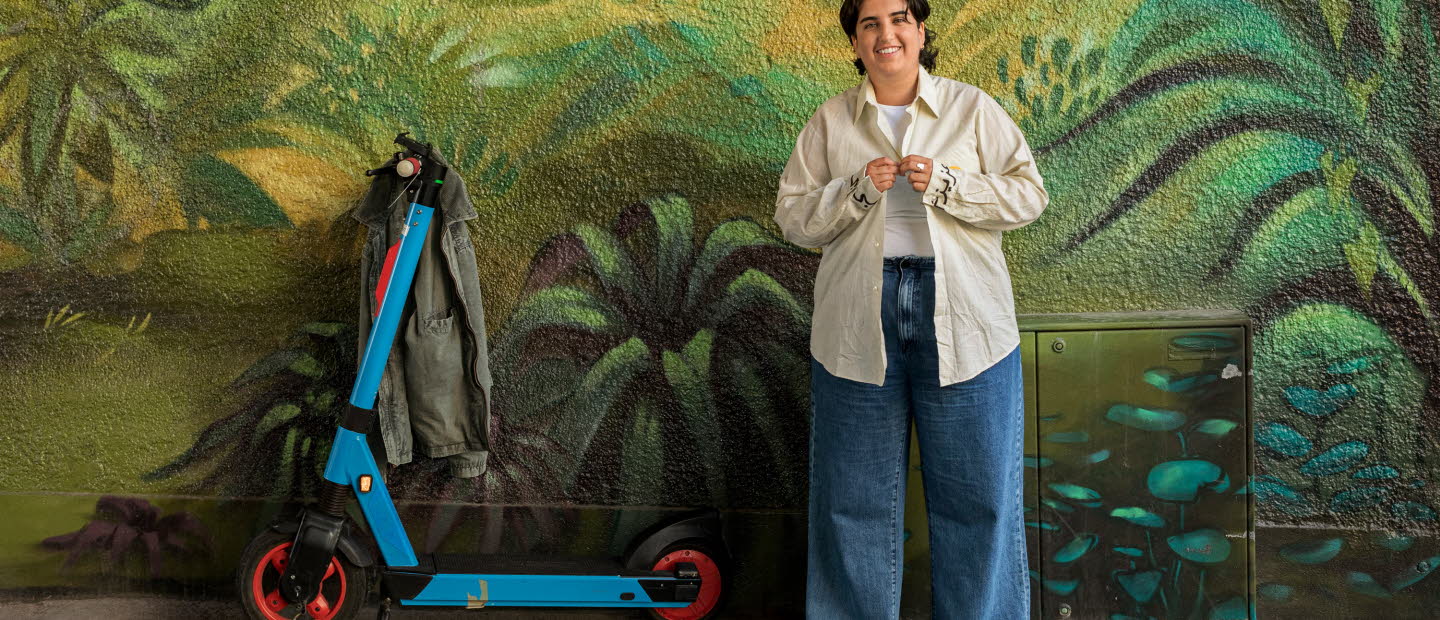 Läsambassadören Nioosha Shams med en sparkcykel framför djungelmålad vägg.