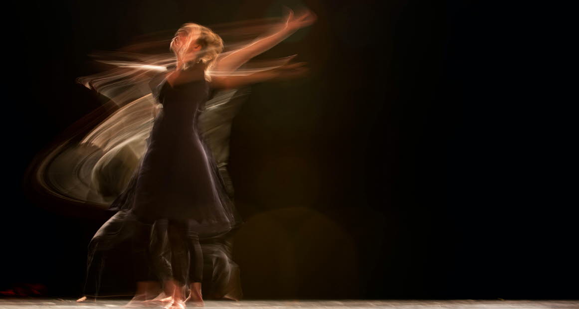 Dansande kvinna fotad med lång slutartid, mörk bakgrund.