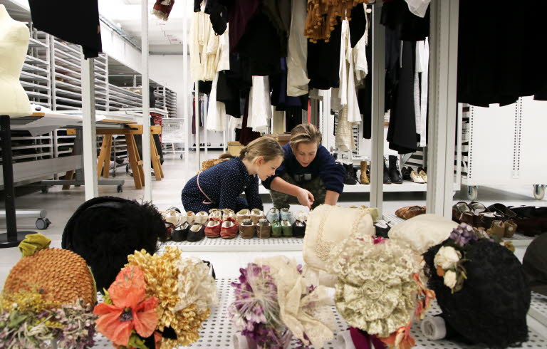 Två barn, pojke och flicka, i museums magasin pekar på samling skor.