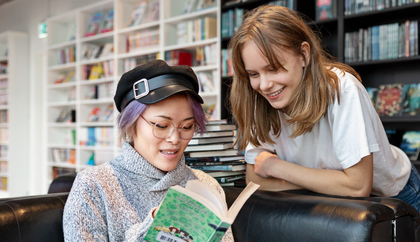 TvÃ¥ ungdomar pÃ¥ ett bibliotek tittar i en bok tillsammans