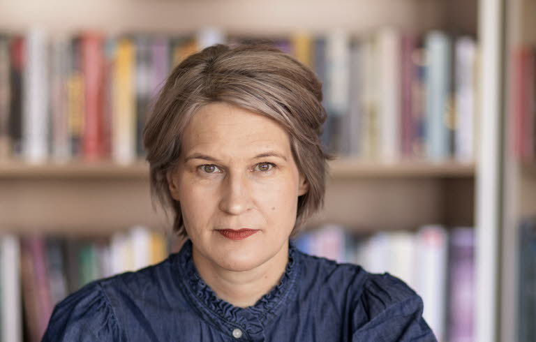 Porträttfotografi av en medelålders kvinna, Kulturrådets generaldirektör. I bakgrunden bokhyllor med böcker.