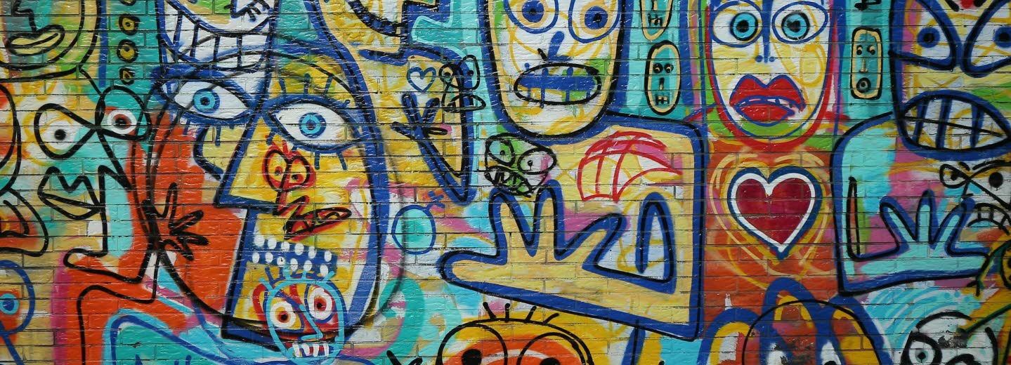 Tegelvägg fylld med grafitti med målade ansikten i glada färger.