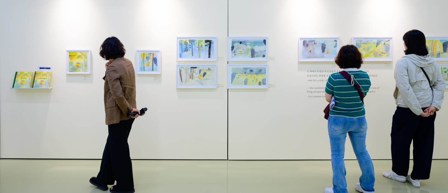 Tre personer tittar på en utställning med teckningar av Eva Lindström under Jeonju internationella bilderboksmässa 2025. Three people are viewing an exhibition of drawings by Eva Lindström at the Jeonju International Picture Book Fair 2025.