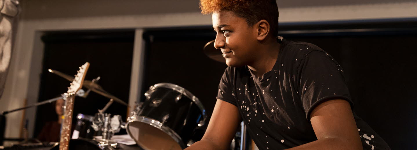 En ung man som sitter vid ett trumset och ler.