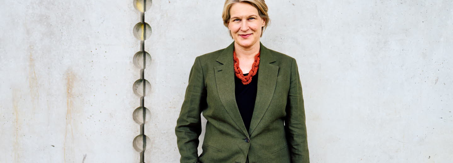Pressbild på Kajsa Ravin som står framför en grå vägg.