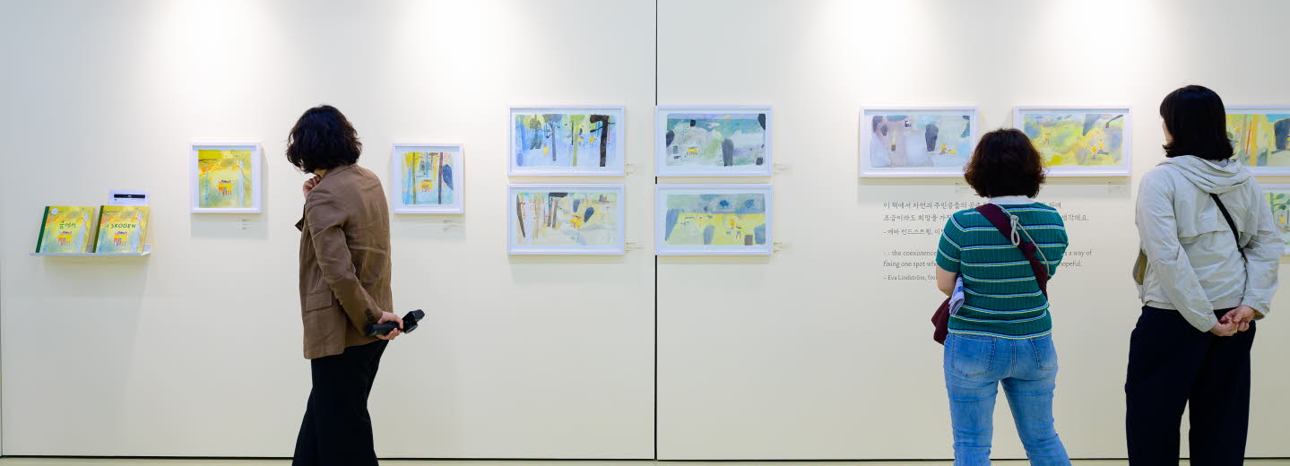 Tre personer tittar på en utställning med teckningar av Eva Lindström under Jeonju internationella bilderboksmässa 2025. Three people are viewing an exhibition of drawings by Eva Lindström at the Jeonju International Picture Book Fair 2025.