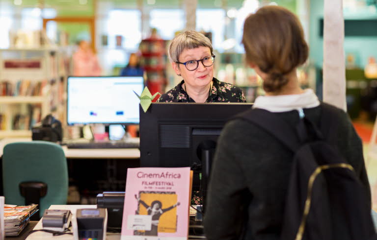 Kvinna som lånar en bok på ett bibliotek.
