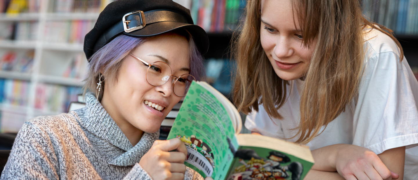 Två ungdomar på ett bibliotek tittar i en bok tillsammans