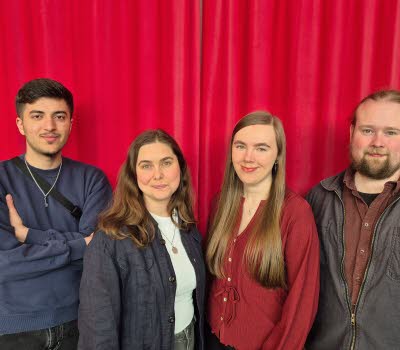 Gruppbild av två kvinnor och två män framför ett rött draperi. 