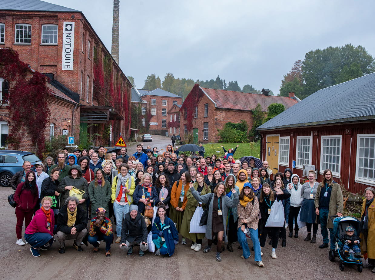 Gruppbild utomhus. I bakgrunden syns ett rött trähus och flera tegelhus.