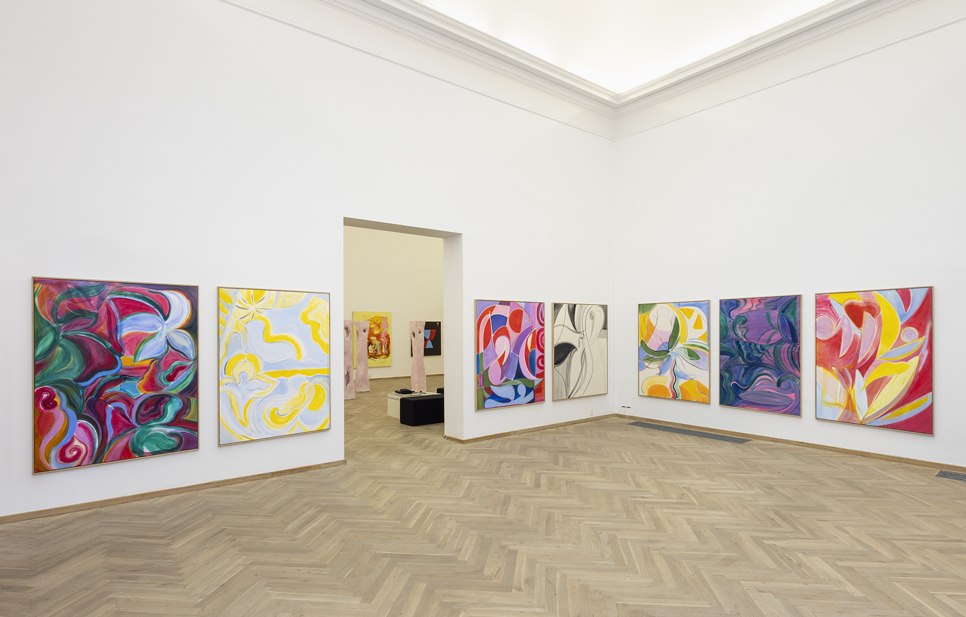 Bild på en utställning med sju stora färgglada målningar.