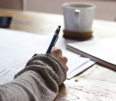 Närbild på en hand som fyller i uppgifter på ett papper. 