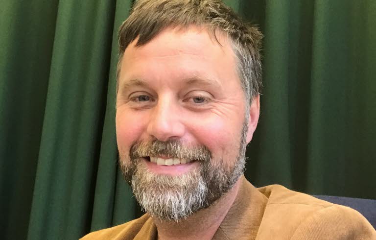 Bild på John Bjerkert, med grön bakgrund.