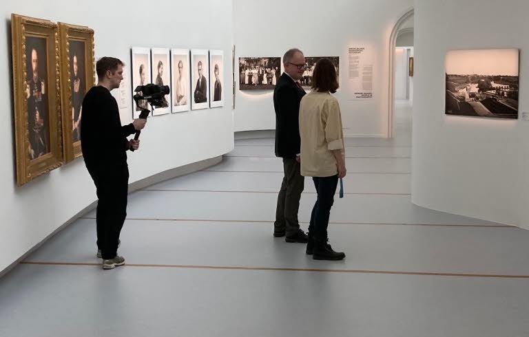 Två personer tittar på konst på Östergötlands museum. I bakgrunden står en filmare och filmar.