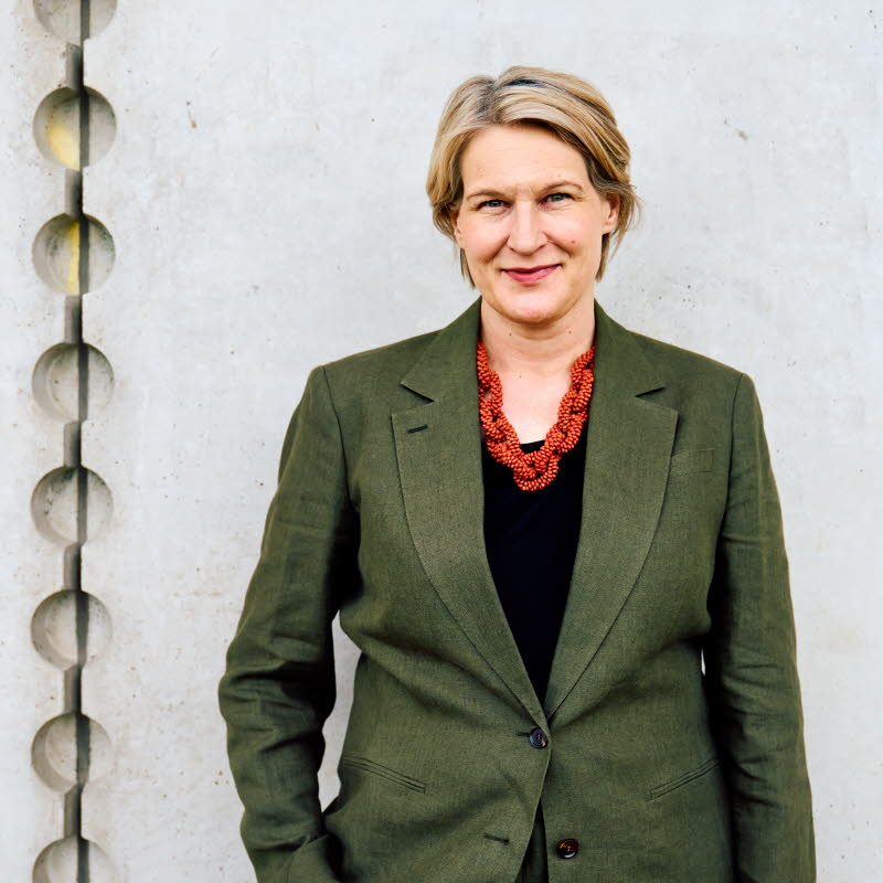 Pressbild på Kajsa Ravin som står framför en grå vägg.