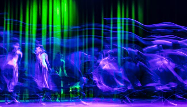 Dansare bakom böljande tyger belysta i blått, grönt och lila.