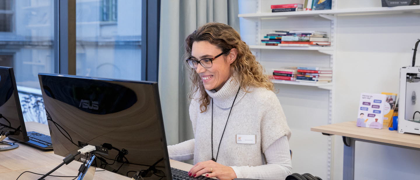 Kvinnlig bibliotekarie sitter framför datorn och tar del samtal som pågår på skärmen.