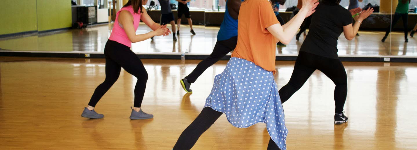 Ungdomar framför stor väggspegel i träningslokal där de tränar dansrörelser. 