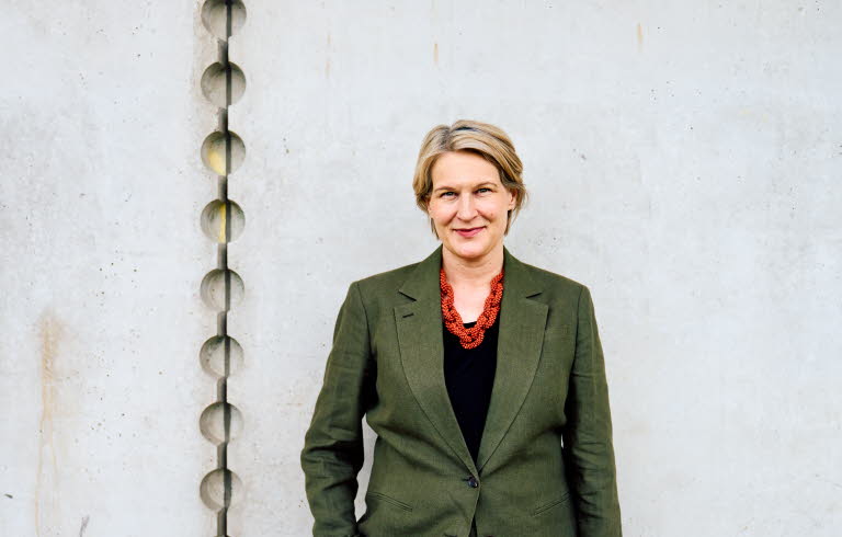 Pressbild på Kajsa Ravin som står framför en grå vägg.