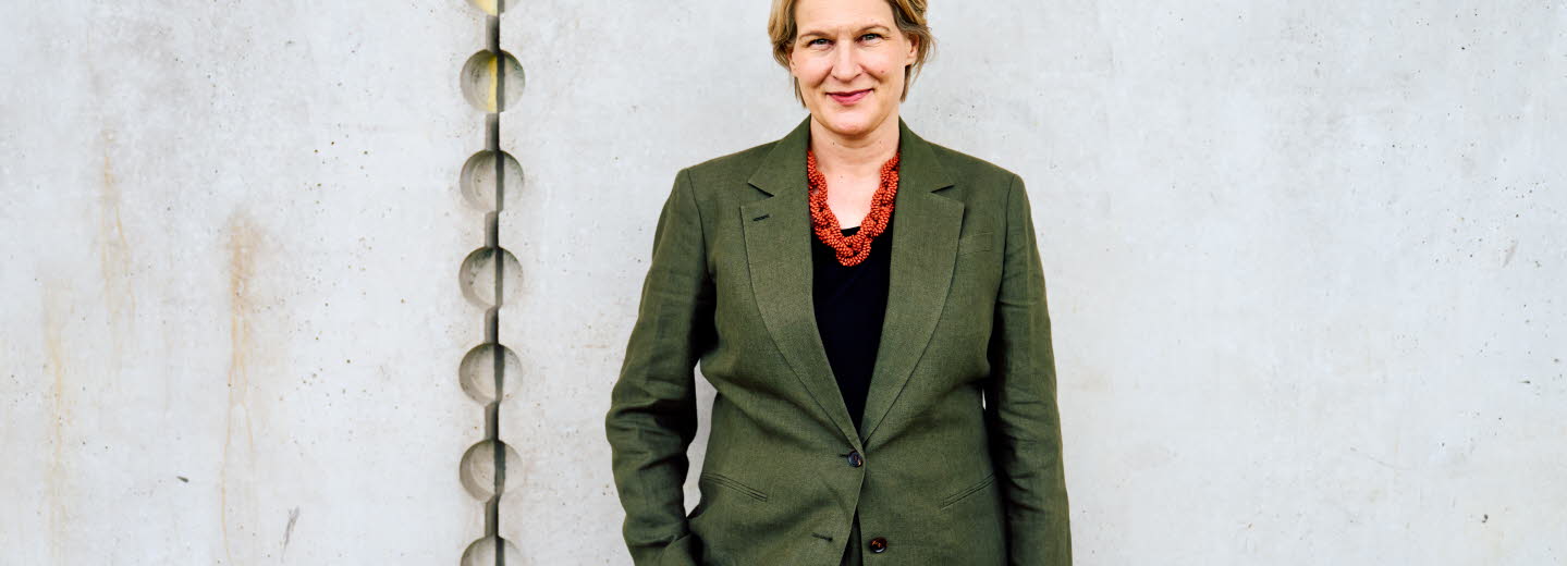 Pressbild på Kajsa Ravin som står framför en grå vägg.