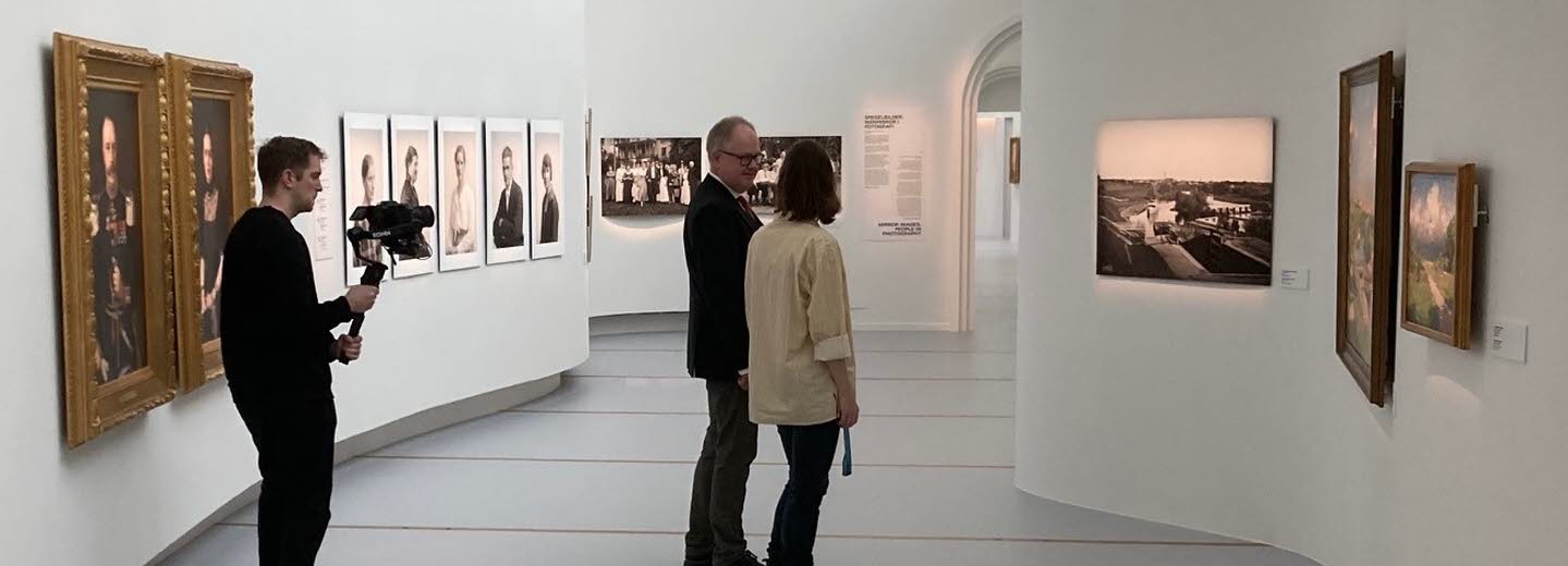 Två personer tittar på konst på Östergötlands museum. I bakgrunden står en filmare och filmar.