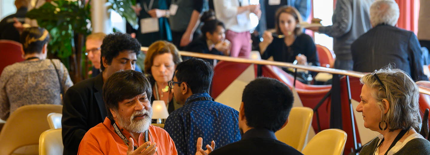 Fullsatt rum med människor som pratar i sittgrupper runt olika bort.