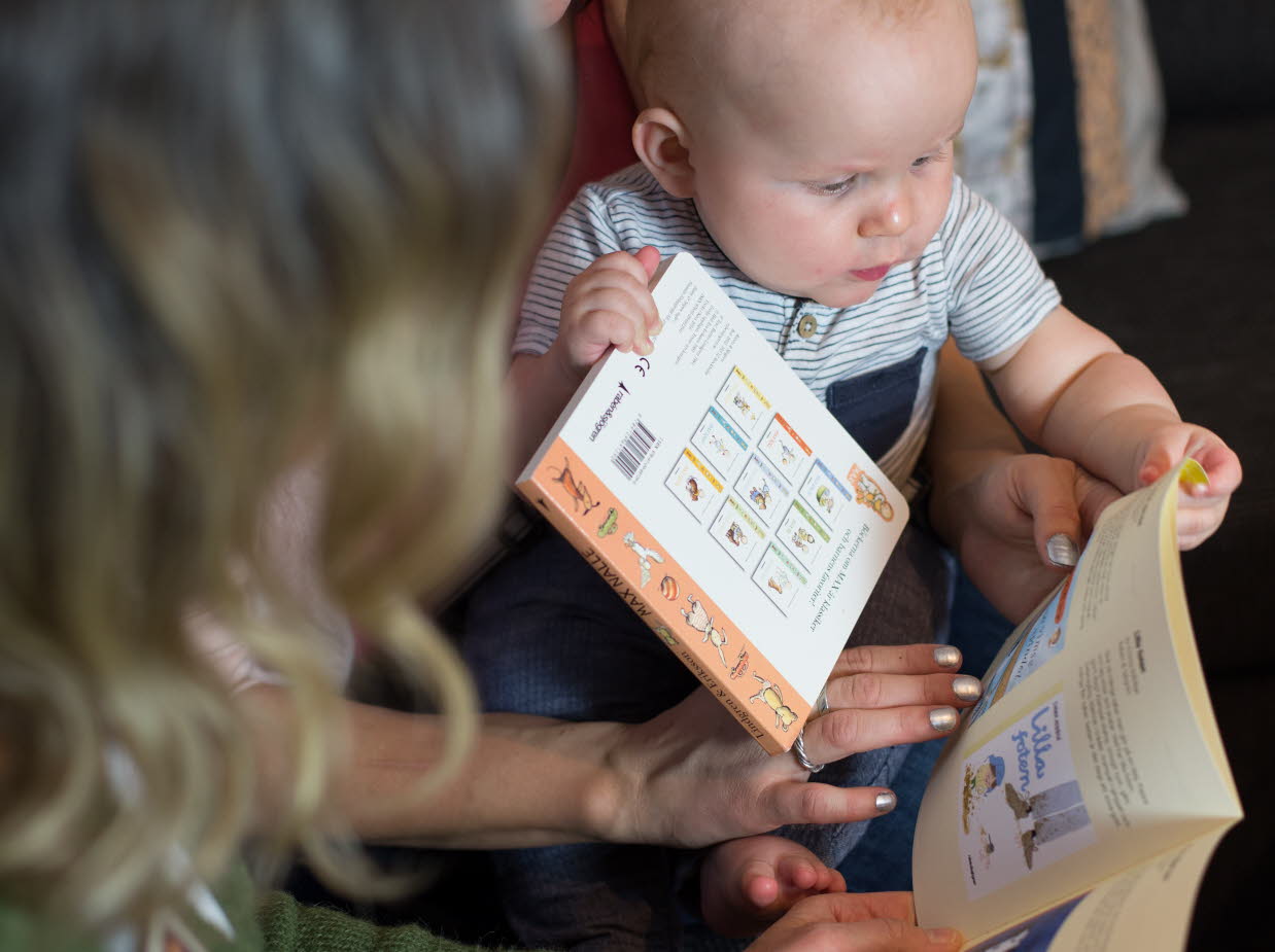 Spädbarn som bläddrar i bok tillsammans med vuxna. Foto: Sara Norling.