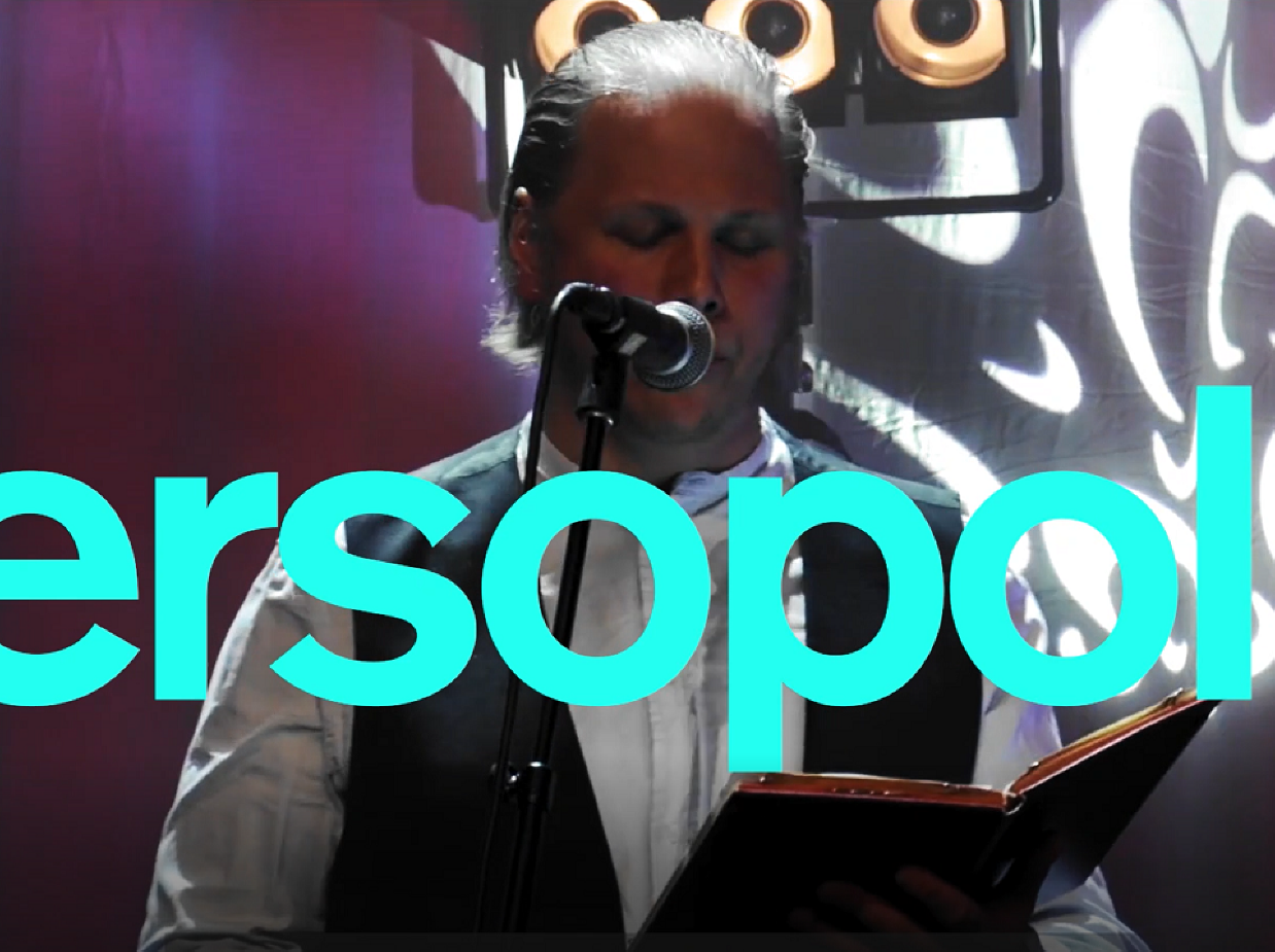 Turkos text med Versopolis, i bakgrunden en man som läser ur en bok på scen..