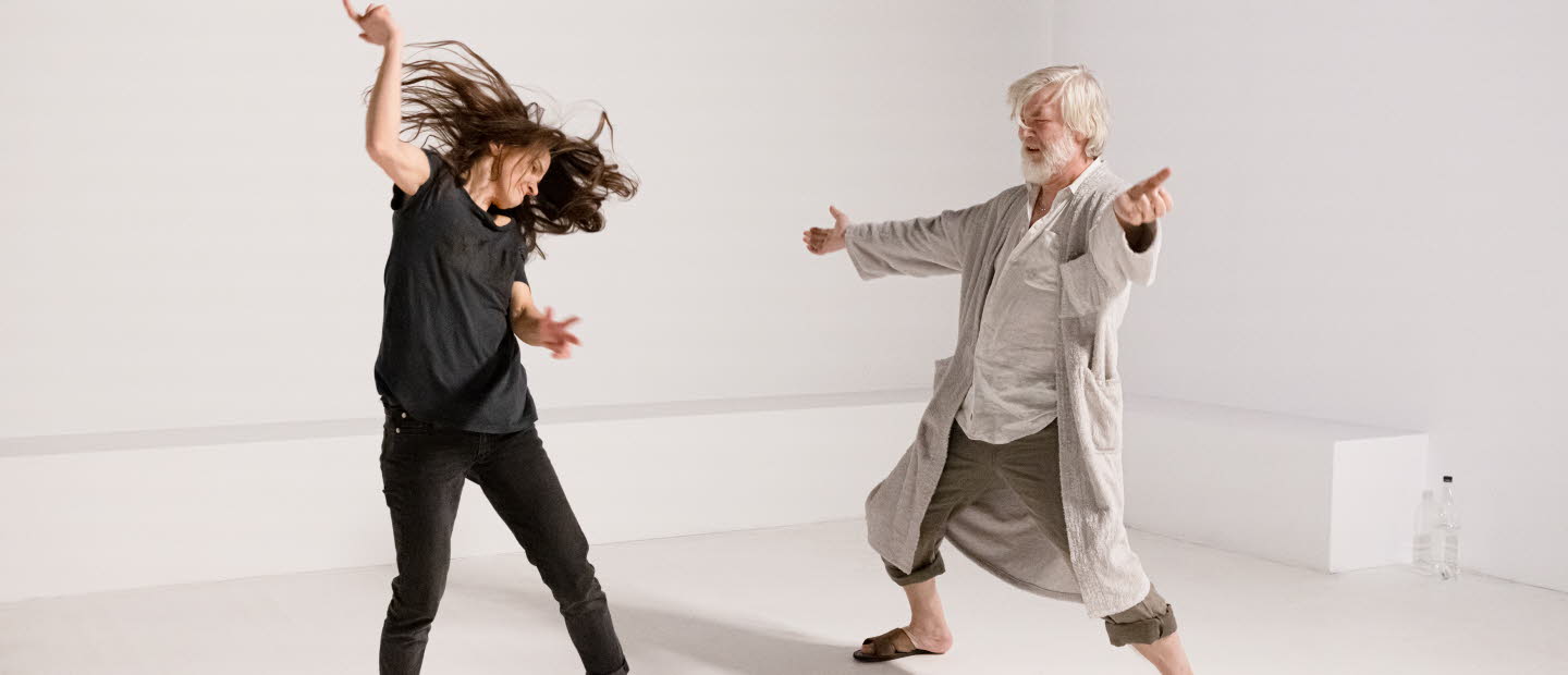 A young woman and an old man are doing a modern dance in a white room.