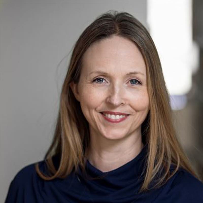 Kvinna i halvfigur omgiven av bokhyllor.