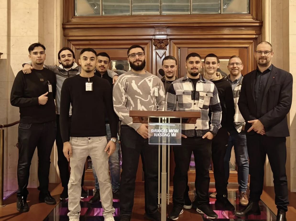 Bild på en grupp mestadels unga män bakom en talarstol som visar att de är i Riksdagen.