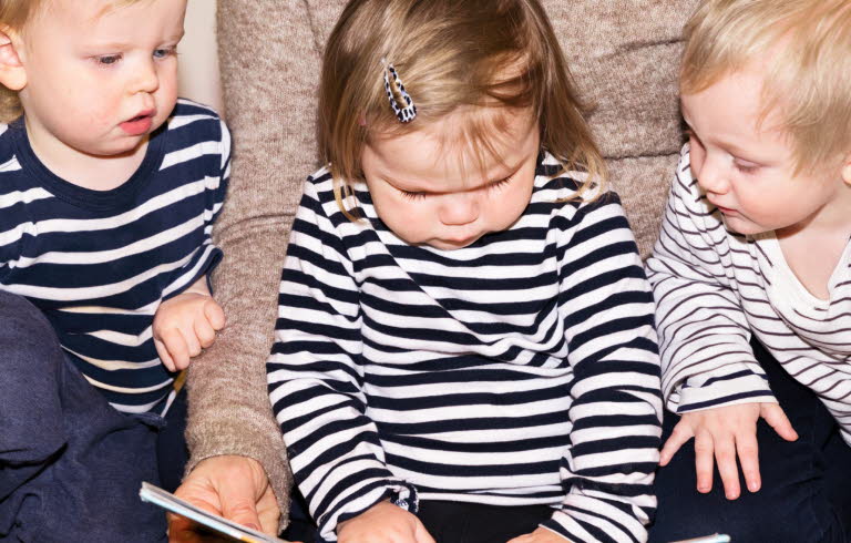 Tre barn som sitter på golvet och bläddrar i en bok. 