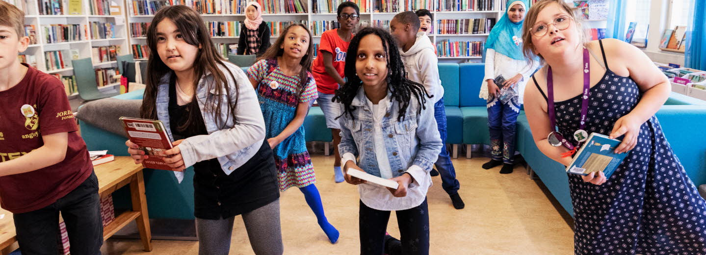Eleverna hoppar, snurrar och gör armhävningar under bokgympan på skolbiblioteket.